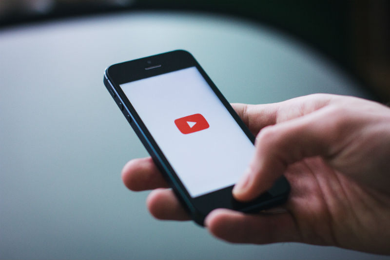 Pessoa com celular na mão usando o youtube para trabalho em home office